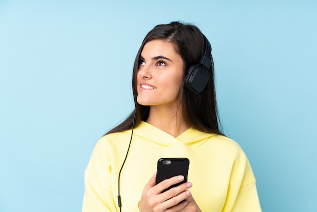 Jovem mulher sobre música de parede azul isolado com um celular e pensamento