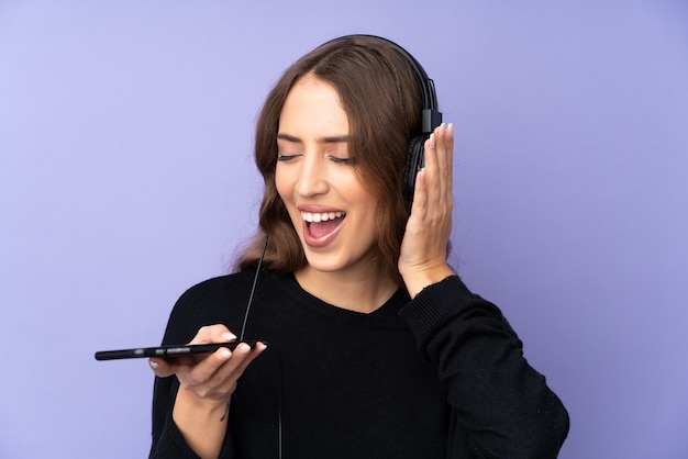 Jovem mulher sobre música de parede roxa isolada com um celular e cantando