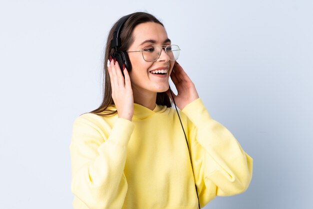 Jovem mulher sobre parede azul isolada, ouvir música e cantar