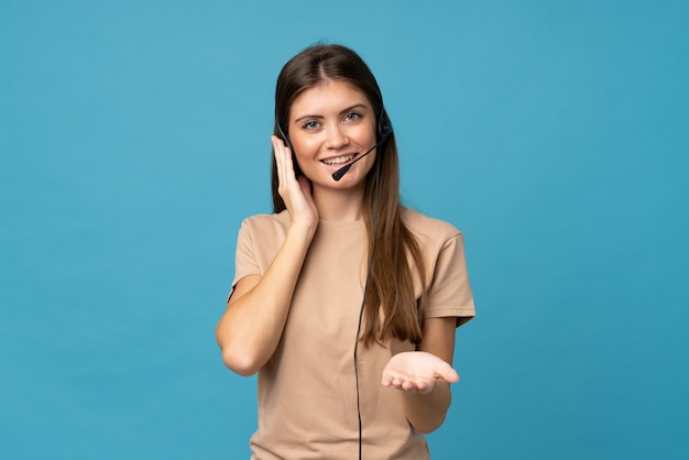 Jovem mulher sobre parede azul isolada, trabalhando com fone de ouvido