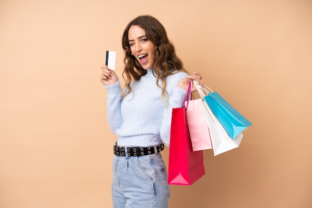 Jovem mulher sobre parede isolada segurando sacolas de compras e um cartão de crédito