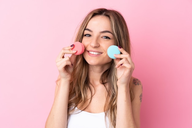 Jovem mulher sobre parede rosa isolada segurando macarons franceses coloridos e sorrindo