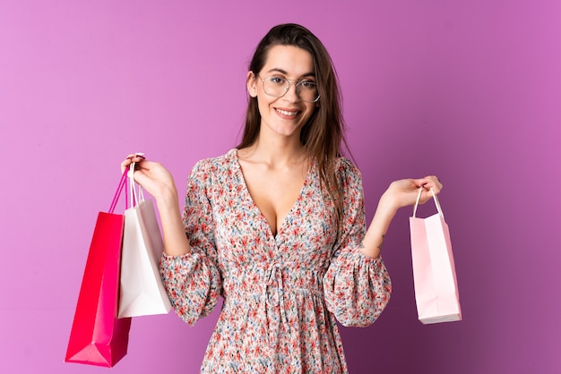 Jovem mulher sobre parede roxa isolada segurando sacolas de compras e sorrindo