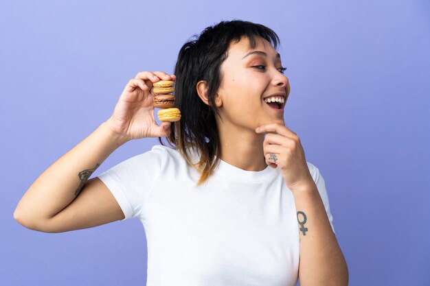 Jovem mulher sobre roxo isolado segurando macarons franceses coloridos e pensando uma idéia