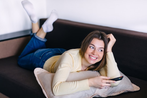 Jovem mulher sorridente assistindo tv enquanto estava deitado em um sofá em casa