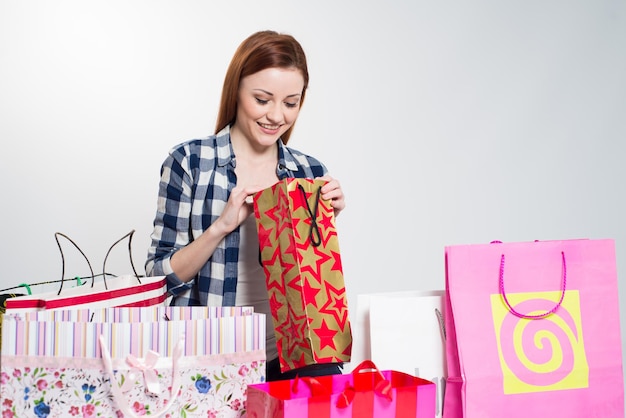 Jovem mulher sorridente atraente com muitas sacolas coloridas em cinza. Mulher fazendo compras