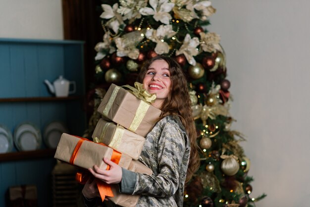 Jovem mulher sorridente de suéter, férias de inverno no interior de casa decorada com árvore de natal.