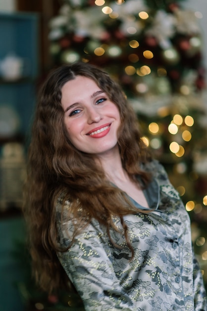 Jovem mulher sorridente de suéter, férias de inverno no interior de casa decorada com árvore de natal.