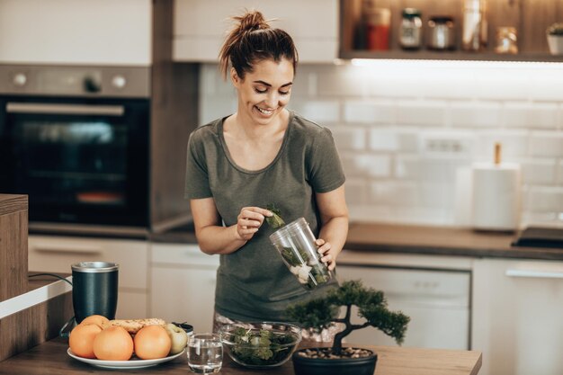 Jovem mulher sorridente fazendo um smoothie saudável na cozinha em casa.