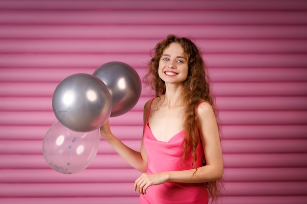 Jovem mulher sorridente positiva recebe presente surpresa e segura nas mãos um balão de ar conceito Black Friday em um fundo rosa