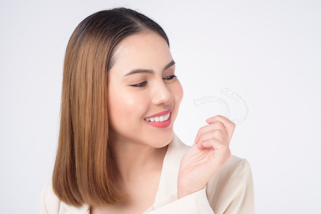 Jovem mulher sorridente segurando aparelho invisalign em estúdio, conceito de saúde odontológica e ortodôntica