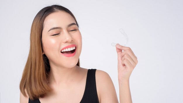 Jovem mulher sorridente segurando aparelho invisalign em estúdio, conceito de saúde odontológica e ortodôntica