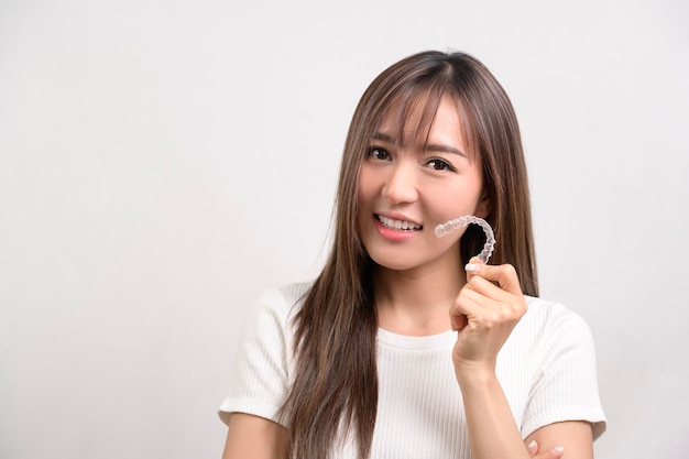 Jovem mulher sorridente segurando aparelho invisalign sobre estúdio de fundo branco