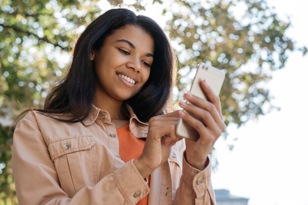 Jovem mulher sorridente segurando smartphone, conversando, comunicação, olhando para a tela digital