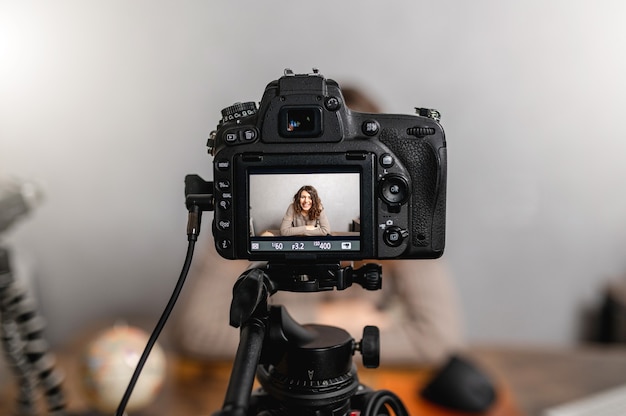 Jovem mulher sorridente, sentado à mesa, falando para a câmera enquanto tirava uma foto. conceito de vlog e freelancer.