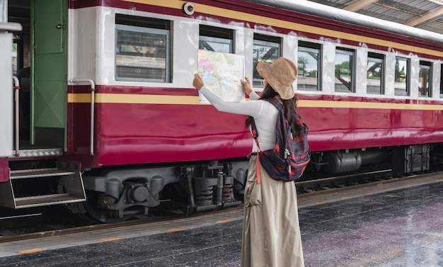 Jovem mulher sorridente viajante com mochila olhando para mapear enquanto espera o trem em