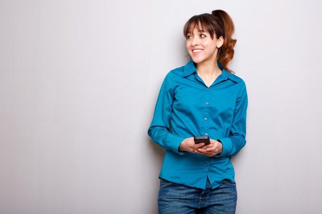 jovem mulher sorrindo com o celular contra um fundo cinzento