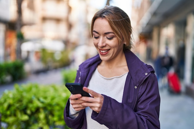 Jovem mulher sorrindo confiante usando smartphone na rua