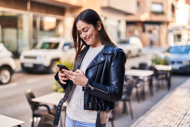 Jovem mulher sorrindo confiante usando smartphone na rua