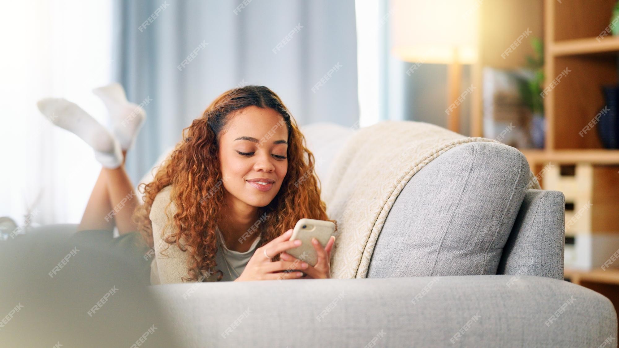 Jovem mulher sorrindo e rindo enquanto envia mensagens de texto em um  telefone em casa mulher alegre conversando com seus amigos com aplicativos  rolando mídias sociais e assistindo memes engraçados da internet enquanto  relaxa em um sofá