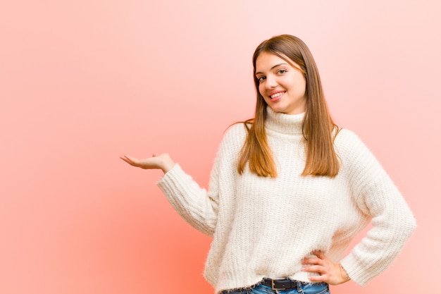 Jovem mulher sorrindo, sentindo-se confiante, bem sucedido e feliz, mostrando o conceito ou idéia no espaço da cópia do lado no rosa