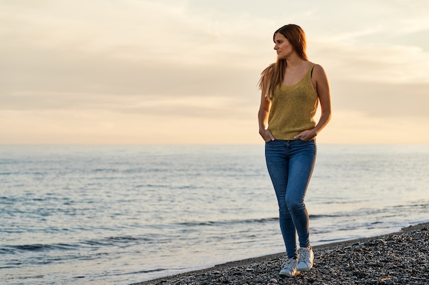 Jovem mulher sozinha caminhando na areia da praia ao pôr do sol. Conceito de relaxamento e meditação