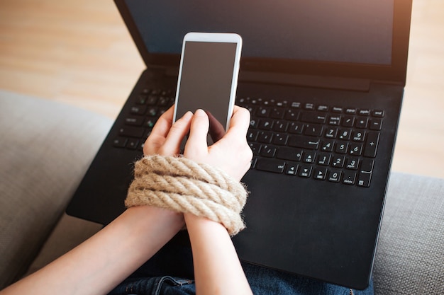 Jovem mulher tem vício em mídias sociais. viciados em laptop de smartphone. corda no pulso. teclado preto.