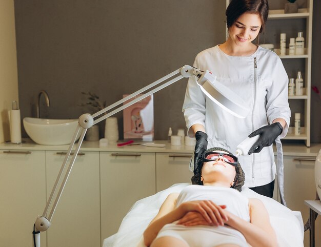 Jovem, mulher, tendo o procedimento de cosmetologia da máquina para o rejuvenescimento do rosto no salão de beleza, cosmetologia e ilustração da foto do conceito anti envelhecimento.