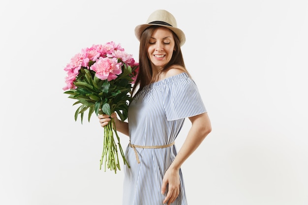 Jovem mulher tenra em um vestido azul, chapéu segurando o buquê de flores de peônias rosa lindas isoladas no fundo branco. dia de são valentim, conceito de feriado do dia internacional da mulher. área de publicidade.