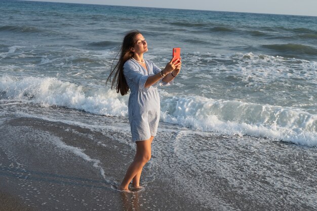 Jovem mulher tirando fotos de si mesma no contexto do mar.