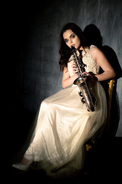 Jovem mulher toca saxofone. Menina com um vestido branco fofo posando com um instrumento musical