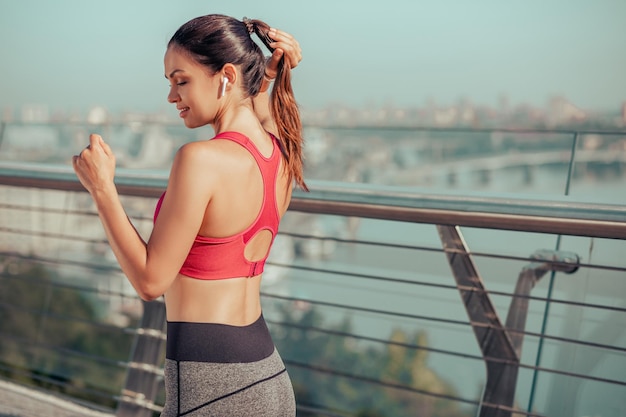 Jovem mulher tocando o cabelo enquanto corre na vista traseira da ponte