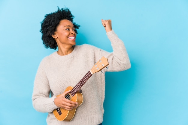 Foto jovem mulher tocando ukelele levantando o punho após uma vitória