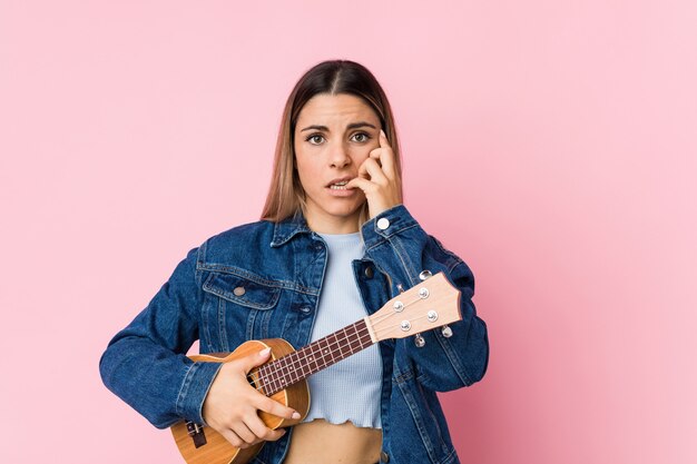 Jovem mulher tocando ukelele roer unhas, nervoso e muito ansioso