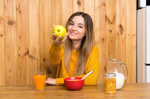 Jovem mulher tomando café da manhã em uma cozinha com uma maçã