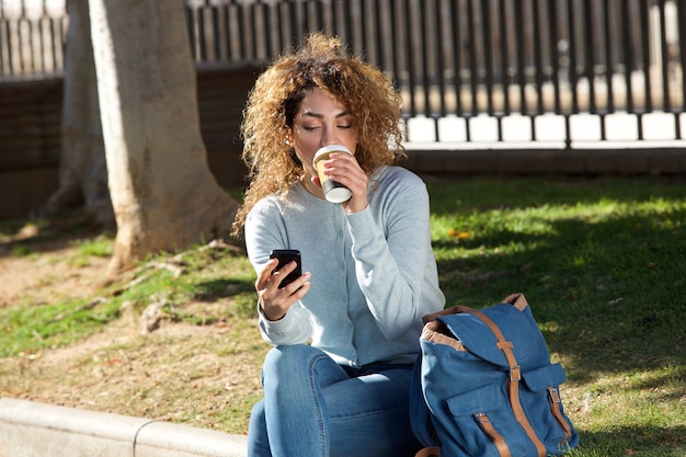 Jovem mulher tomando café e olhando para celular