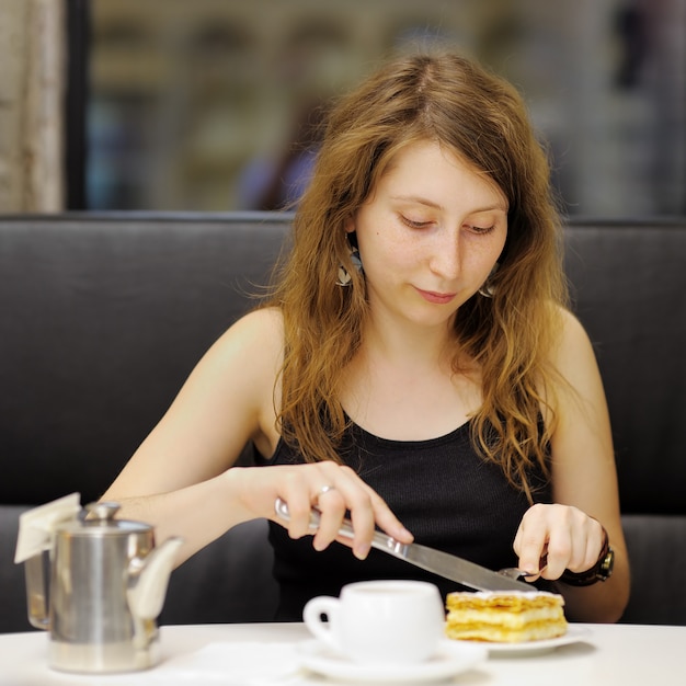 Jovem mulher tomando chá e sobremesa em um café