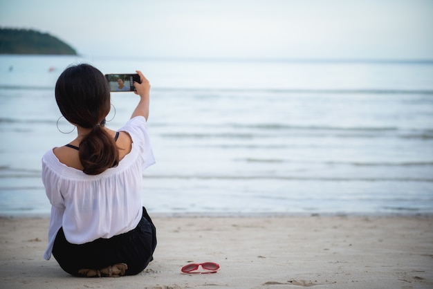 Foto jovem mulher tomando uma selfie com um telefone em uma bela praia.