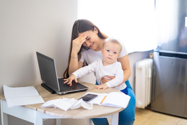 Foto jovem mulher trabalhando em casa com um laptop com um bebê nas mãos