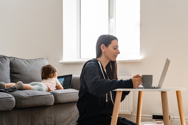 Jovem mulher trabalhando em casa. Criança assistindo desenhos sobre o tablet. Trabalho a partir de casa