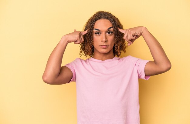 Jovem mulher transexual latina isolada em fundo amarelo, focada em uma tarefa, mantendo os indicadores apontando a cabeça.