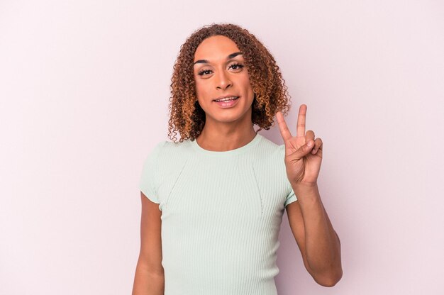 Foto jovem mulher transexual latina isolada no fundo rosa alegre e despreocupada, mostrando um símbolo da paz com os dedos.