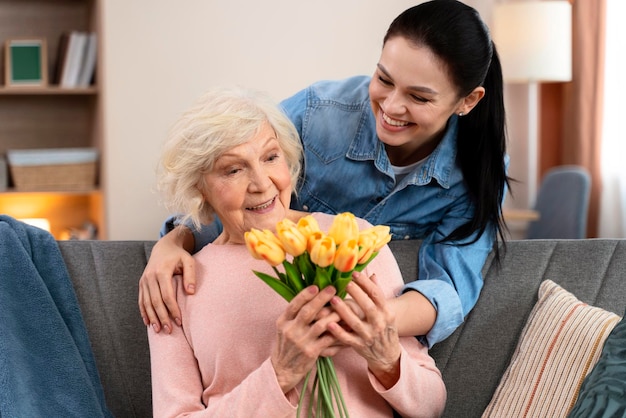 Jovem mulher trazendo flores para sua mãe sênior em casa Relações entre mãe e filha Comemorando o conceito feliz do dia das mães