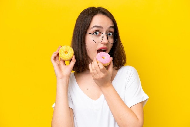 Jovem mulher ucraniana isolada em fundo amarelo comendo um donut