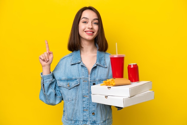 Jovem mulher ucraniana segurando fast-food isolada em fundo amarelo mostrando e levantando um dedo em sinal do melhor