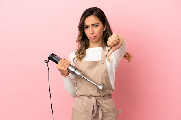 Jovem mulher usando a varinha mágica sobre fundo rosa isolado, mostrando o polegar para baixo com expressão negativa