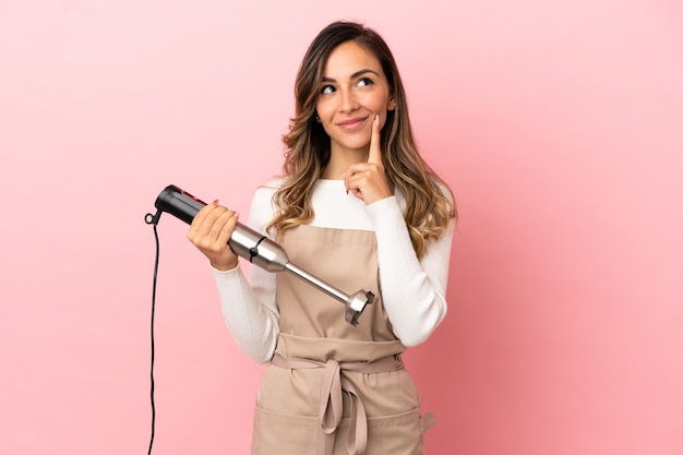 Jovem mulher usando a varinha mágica sobre um fundo rosa isolado, pensando em uma ideia enquanto olha para cima