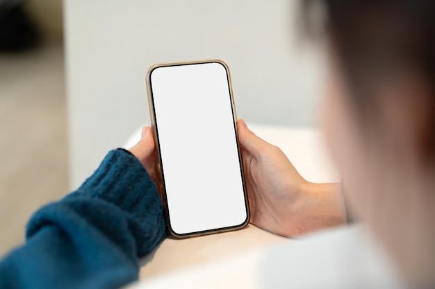 Jovem mulher usando design moderno sem moldura de tela em branco do smartphone enquanto estava deitado na cama no interior de casa