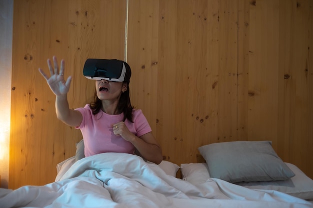 Jovem mulher usando fone de ouvido de realidade virtual na cama VR Futuro jogo de tecnologia digital filmes entretenimento metaverso NFT e conceito de ciberespaço 3D
