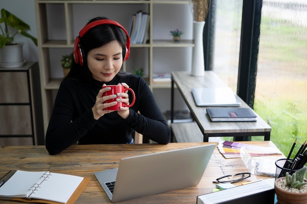 Jovem mulher usando fone de ouvido e bebendo café quente no escritório.